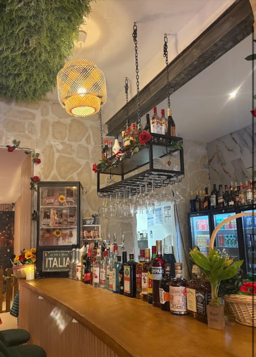 Bar du restaurant italien La Pasta Della Mama à Nice : mur en pierre, verres suspendus et plaque « La vita è bella »